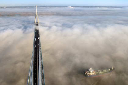 France, entre Calvados (14) et Seine-Maritime (76), cargo passant sous le Pont de Normandie qui émerge des brumes matinales de l'automne et enjambe la Seine, la Réserve Naturelle de l'estuaire de la Seine en arrière plan, vue depuis le sommet du pylone sud