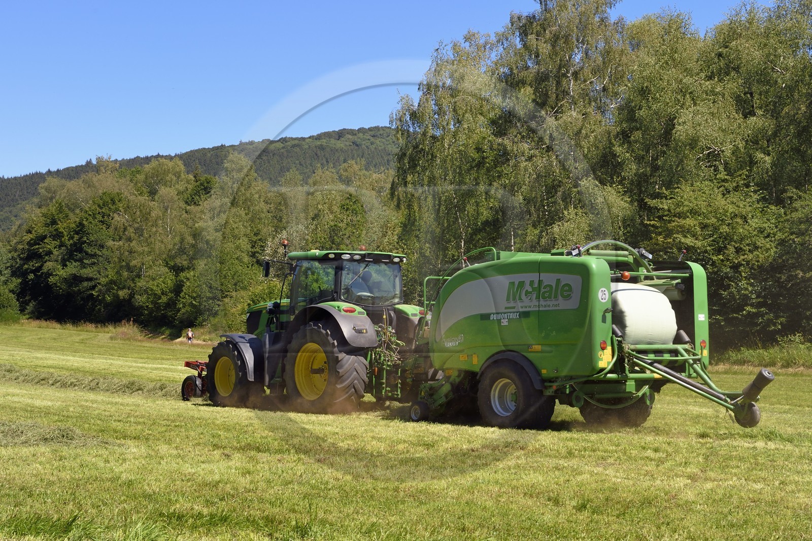 France, Puy-de-Dôme (63), Saint-Ours-les-Roches, hameau de Beauregard, tracteur récoltant le fourrage avec une presse enrubanneuse de balles de foin dans un champ