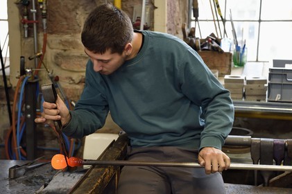 France, Moselle (57), Meisenthal, Centre international d’Art verrier (CIAV), l'atelier de soufflage, fabrication artisanale d'une boule de Noël, le souffleur régularise la masse au marbre tout en effectuant une rotation continue de sa canne et préparation de la paraison avant le passage au moule