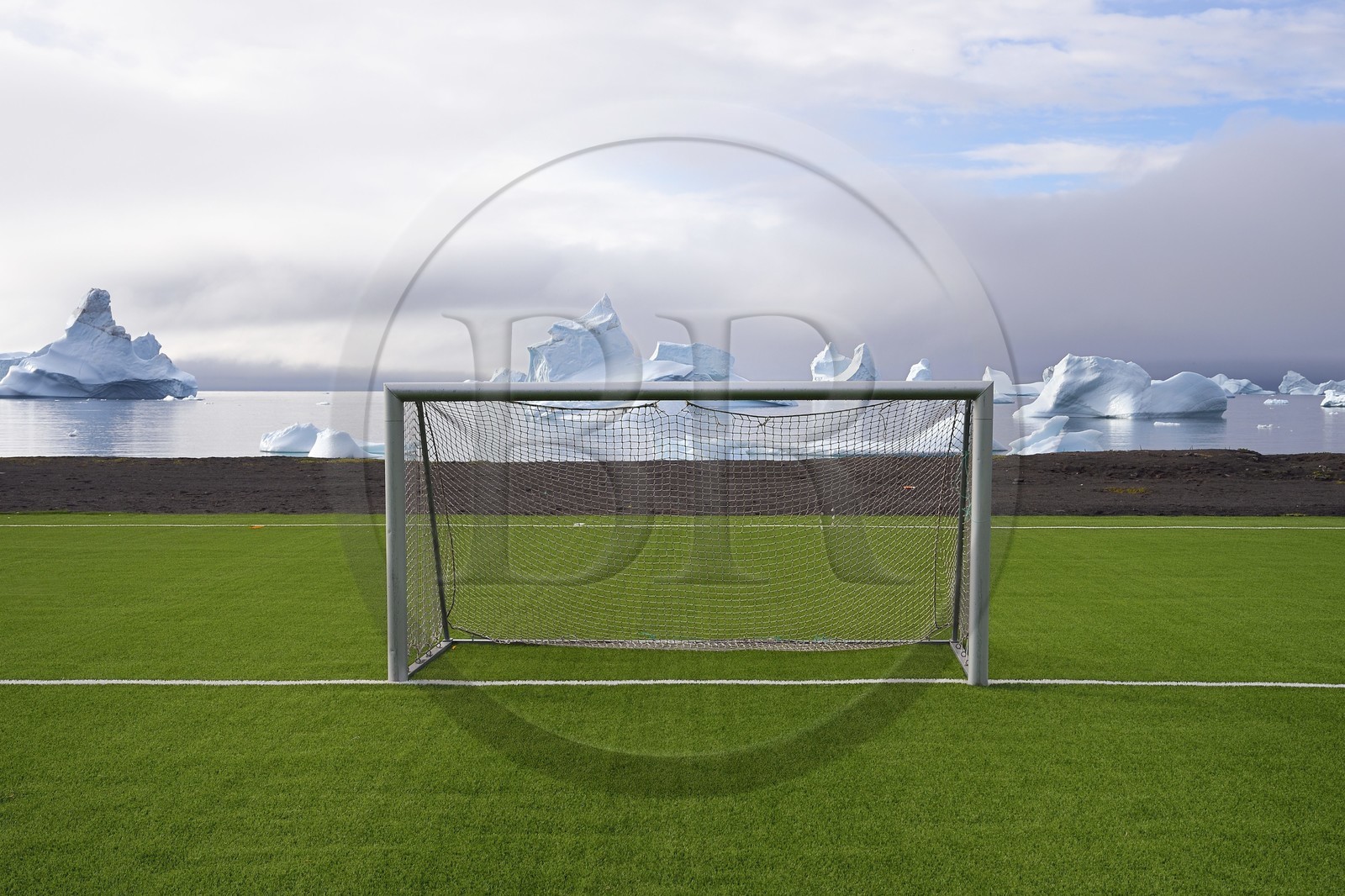 Groenland, cote ouest, Ile de Disko, Qeqertarsuaq, cage du but du terrain de football recouvert d'herbe synthétique et icebergs en arrière plan