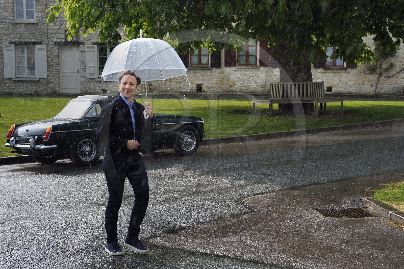 France, Yvelines (78), Montchauvet, tournage pour la télévision du Village Préféré des Français avec Stéphane Bern, Stéphane Bern sous la pluie sur la place de l'église