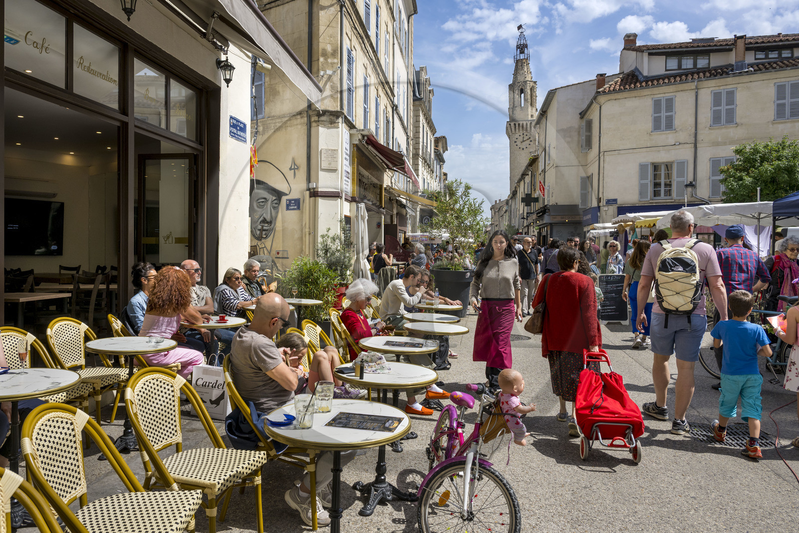 France, Vaucluse (84), Avignon, terrasses de café sur la place du Portail Matheron un jour de marché, un portrait de Raimu lors de la partie de cartes du film Marius de Marcel Pagnol par l'artiste graffeur Lekto, le clocher des Augustins en arrière plan