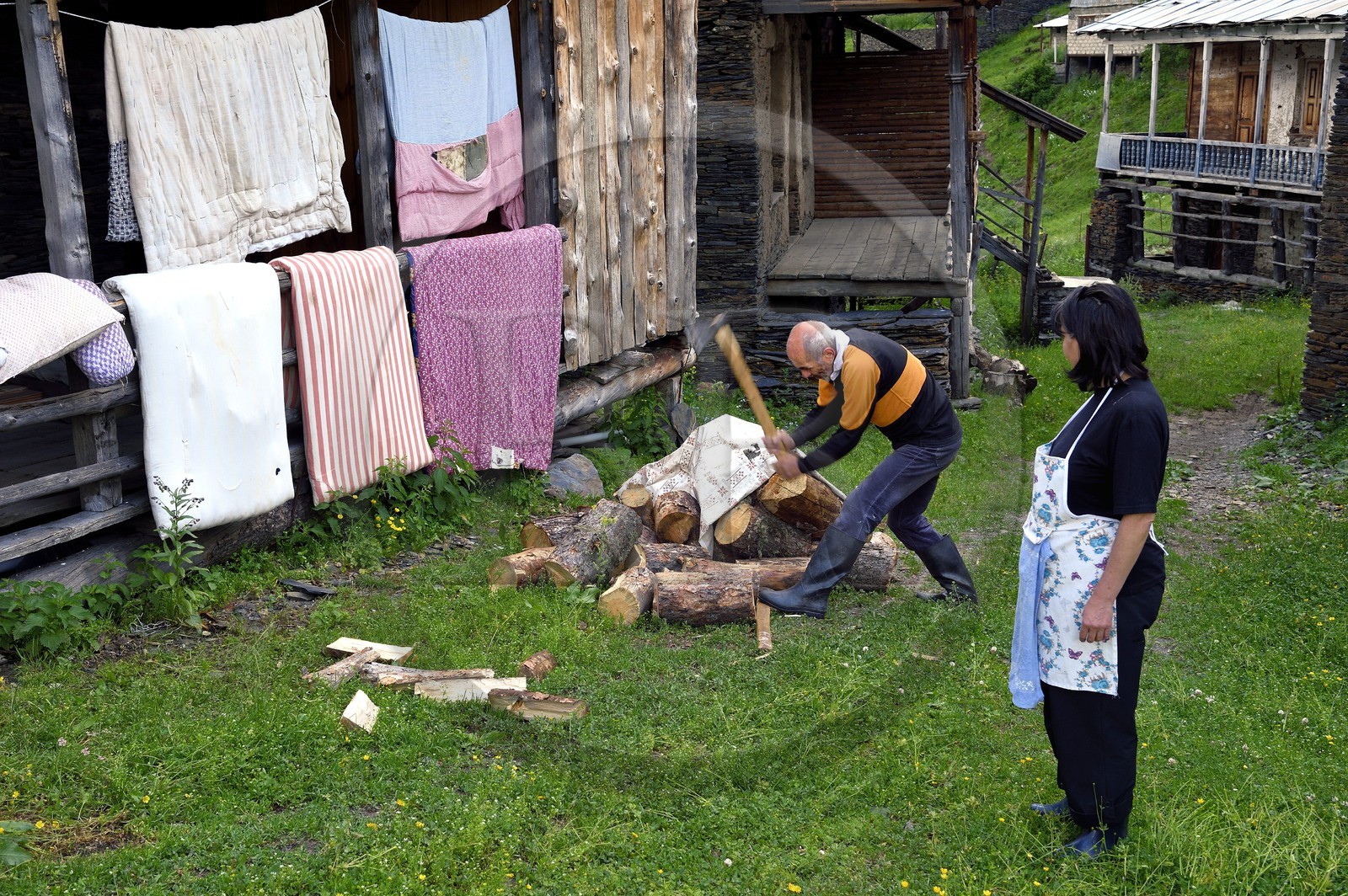 Géorgie, Kakheti, Parc national de Touchétie, village de Shenako, Soso Pirashvili qui fend le bois et Lia Otarashvili devant leur maison d'été