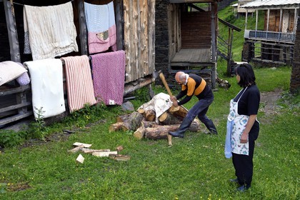 Géorgie, Kakheti, Parc national de Touchétie, village de Shenako, Soso Pirashvili qui fend le bois et Lia Otarashvili devant leur maison d'été