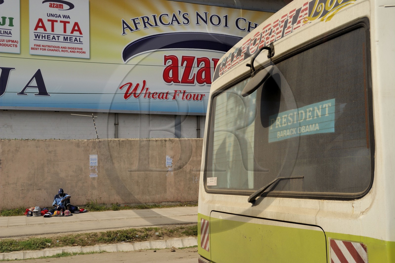Tanzanie, Dar es-Salaam, vendeur de casquettes sur le trottoir et affiche de Barack Obama à l'arrière d'un bus