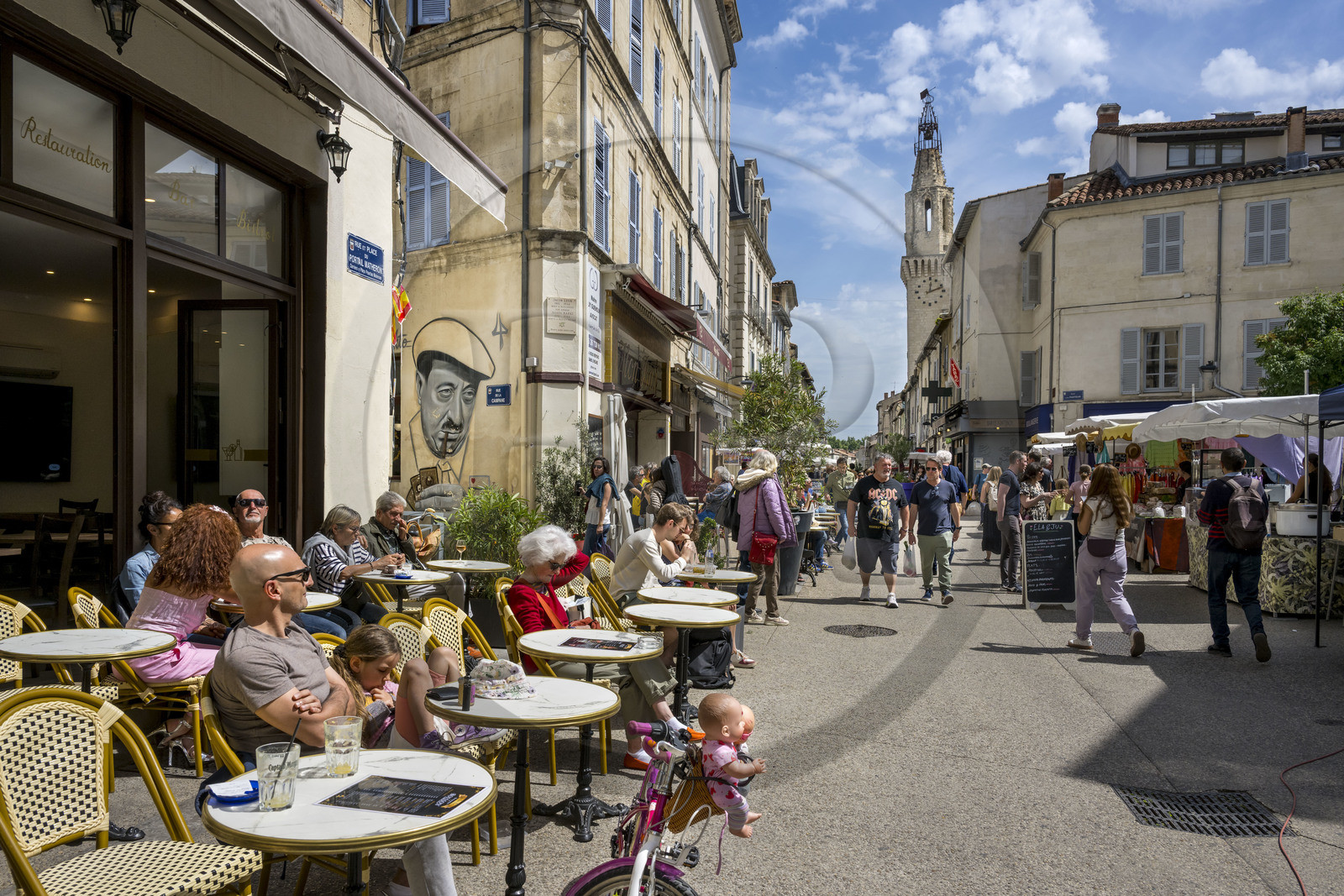 France, Vaucluse (84), Avignon, terrasses de café sur la place du Portail Matheron un jour de marché, un portrait de Raimu lors de la partie de cartes du film Marius de Marcel Pagnol par l'artiste graffeur Lekto, le clocher des Augustins en arrière plan