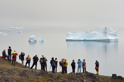 Groenland, cote ouest, Ile de Disko, Qeqertarsuaq, randonneurs sur la côte et icebergs dans la brume en arrière plan