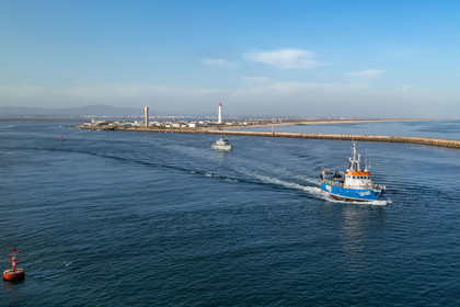 Portugal, Algarve, Parc naturel de la Ria Formosa, Faro, bateau de pêche sortant du port, le phare de Ilha do Farol sur Ilha da Culatra en arrière plan (vue aérienne)
