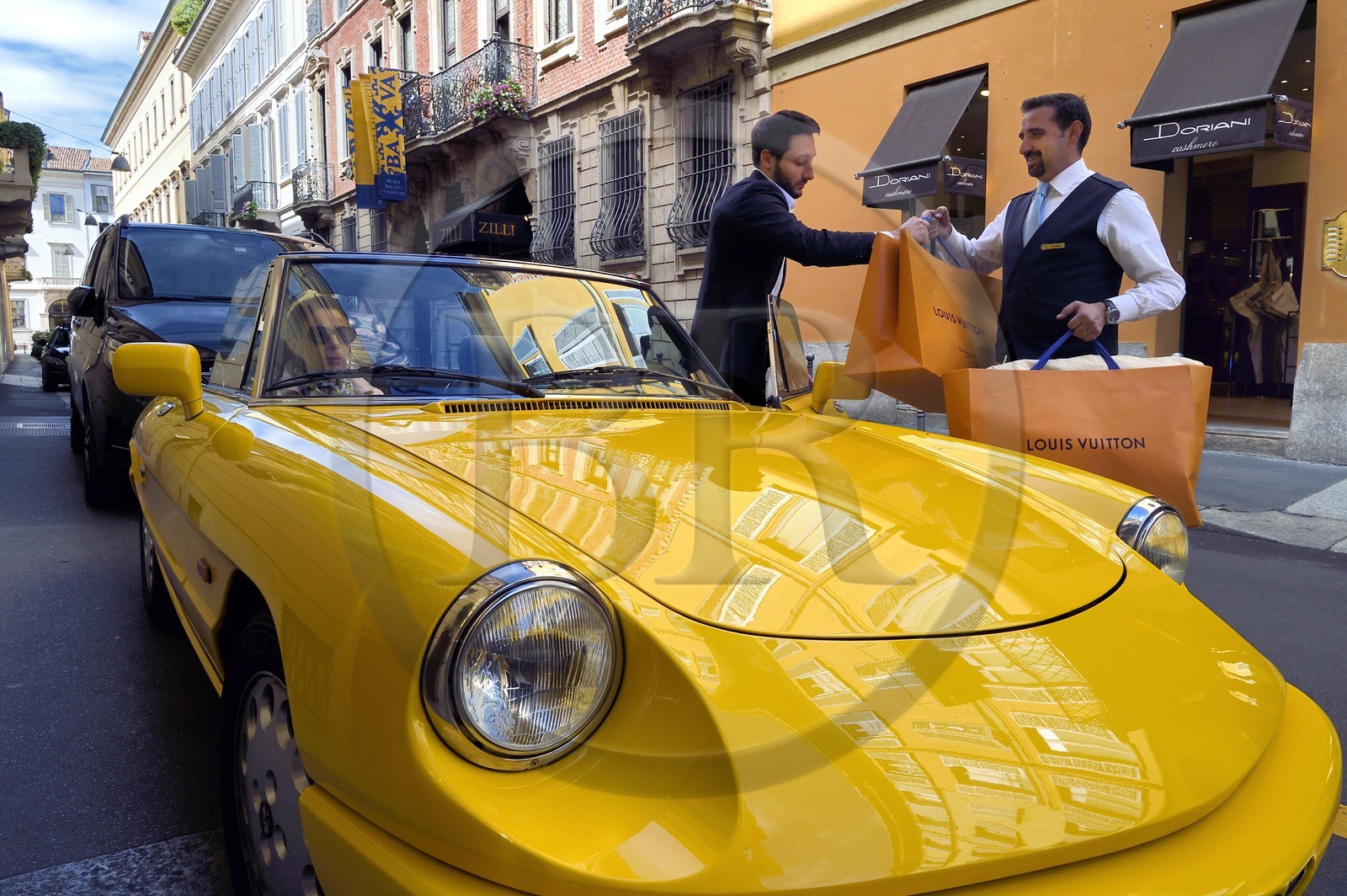 Italie, Lombardie, Milan, Quadrilatère de la Mode (Quadrilatero della moda), cabriolet Alfa Romeo Duetto Spider jaune devant le Four Seasons Hotel Milano, le portier amène un sac Vuitton