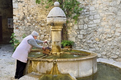 France, Alpes-Maritimes (06), Peille, femme remplissant une bonbonne à la fontaine place du Mont Agel