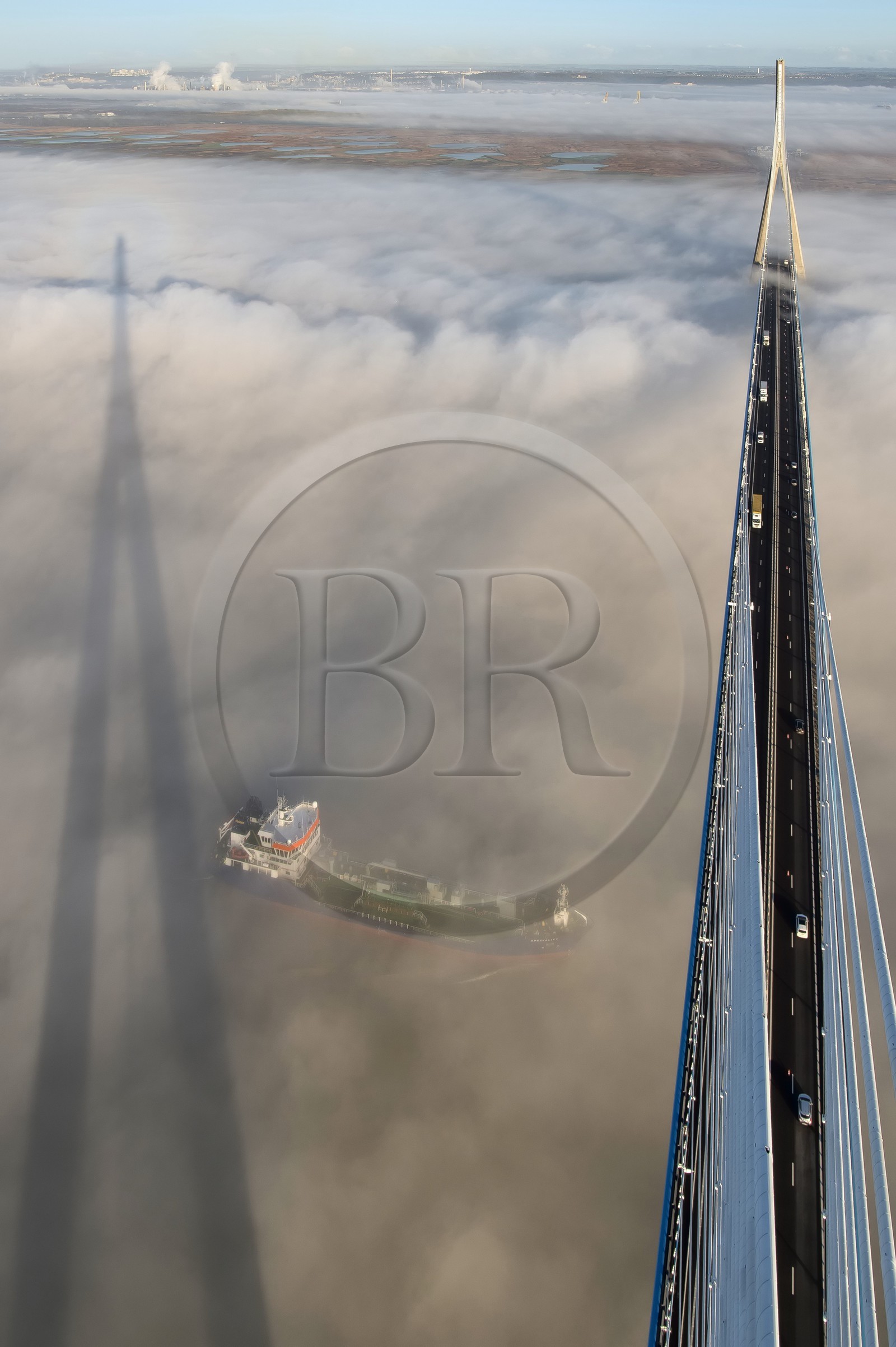 France, entre Calvados (14) et Seine-Maritime (76), cargo passant sous le Pont de Normandie qui émerge des brumes matinales de l'automne et enjambe la Seine, la Réserve Naturelle de l'estuaire de la Seine en arrière plan, vue depuis le sommet du pylone sud