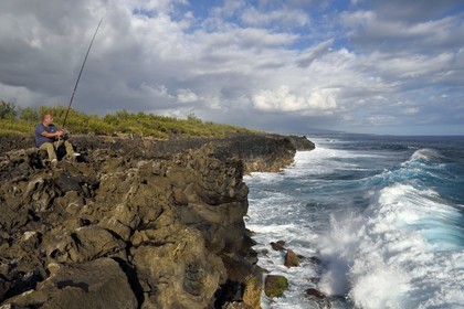 France, Ile de la Reunion, L'Etang Salé les Bains, la côte entre Le Gouffre et l'Etang du Gol, roches noires basaltiques d'origine volcanique tourmentées par l'océan, pêcheur à la ligne
