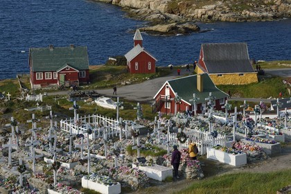 Groenland, cote ouest, baie de Baffin, Upernavik, le cimetière, les cercueils sont déposés en surface puis recouverts de pierres ou de ciment, le sol ne pouvant être creusé, les tombes sont ensuite décorées avec des fleurs artificielles, l'ancienne église et les batiments du musée en arrière plan