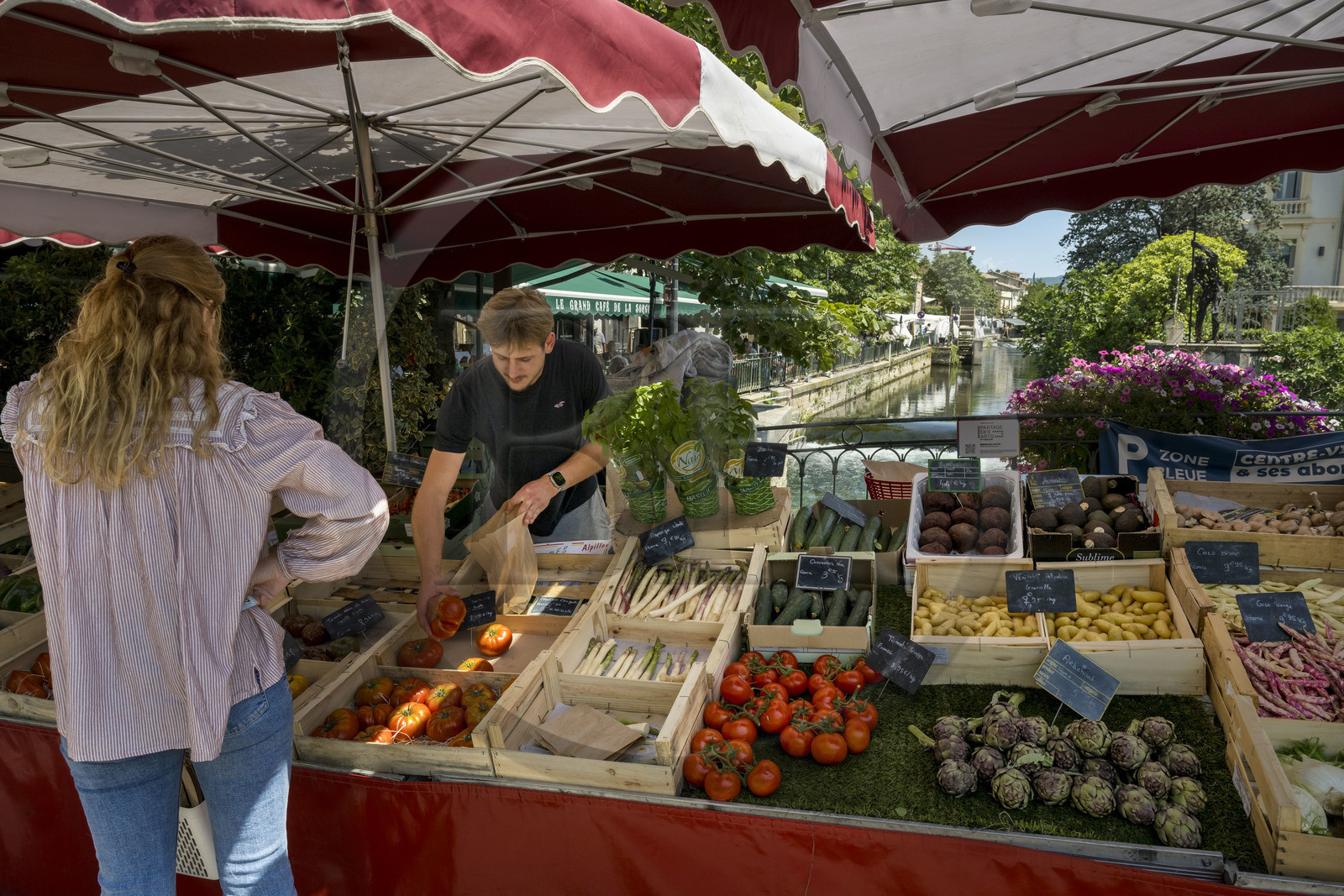 France, Vaucluse (84), L'Isle-sur-la-Sorgue, jour de marché, Justin sert une cliente de son étal de fruits et légumes sur un pont de la Sorgue