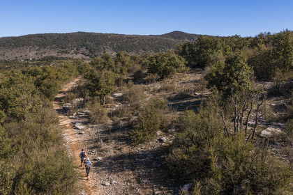 France, Hérault (34), les Causses et les Cévennes, paysage culturel de l'agro-pastoralisme méditerranéen inscrit au Patrimoine Mondial de l'UNESCO, Saint-Maurice-Navacelles, randonneurs progressant sur le GR 7 dans un paysage typique du causse du Larzac, le massif de la Séranne qui s'est formé sur une barrière corallienne en arrière plan (vue aérienne)