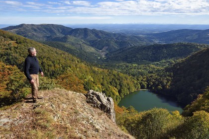 France, Vosges (88), Parc naturel régional des ballons des Vosges, Saint-Maurice-sur-Moselle, randonneur au sommet de la Tete des Perches au dessus de Gazon Rouge, le Lac des Perches, la plaine d'Alsace et les Alpes en arrière plan